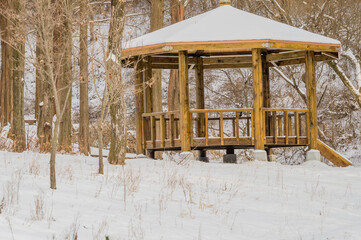 Fototapeta na wymiar Winter landscape of a gazebo in a park surrounded by trees and the roof and ground covered with snow