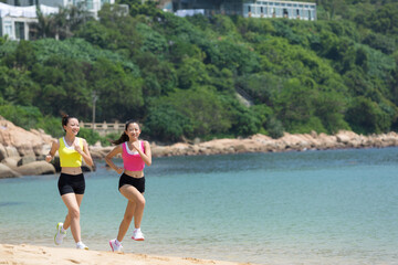 Two female friends running along the sea