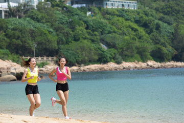 Two female friends running along the sea