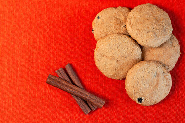 Oatmeal cookies with raisins and cinnamon sticks on orange textured linen cloth background, copy...