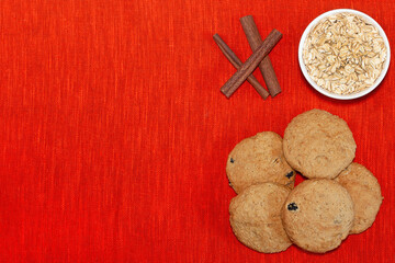 Oatmeal cookies with raisins, oat flakes and cinnamon sticks on orange textured linen fabric...