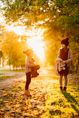 bright sun rays. little sisters with plush toys hats walking in autumn Park.