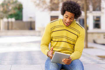 Fototapeta premium Black man using a digital tablet sitting on a bench outdoors.