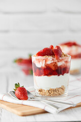 Homemade layered dessert with fresh strawberries, cream cheese or yogurt, granola and strawberry jam in glasses on white wood background. Healthy organic breakfast or snack concept. Selective focus.