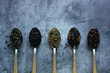 Various types of herbal tea in spoons. Spoons with dry tea leaves. Tea on a concrete background