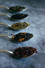 Various types of herbal tea in spoons. Spoons with dry tea leaves. Tea on a concrete background