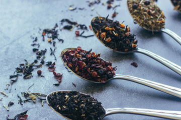 Various types of herbal tea in spoons. Spoons with dry tea leaves. Tea on a concrete background