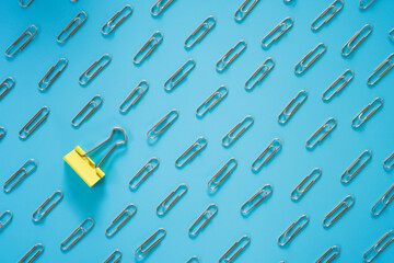 Yellow paper clip laid among steel paper clip on blue background , differentiation concept