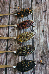 Various types of herbal tea in spoons. Spoons with dry tea leaves. Tea on a wooden background