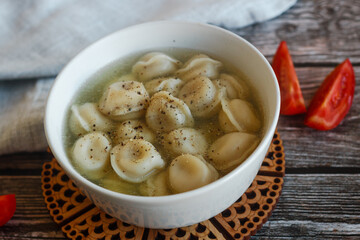 Dumplings with broth in a plate. Traditional Russian dish. Pelmeni with tomatoes on a wooden table