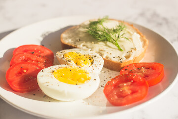 Delicious breakfast on the table. Boiled eggs, tomatoes, cream cheese sandwich, dill on a plate