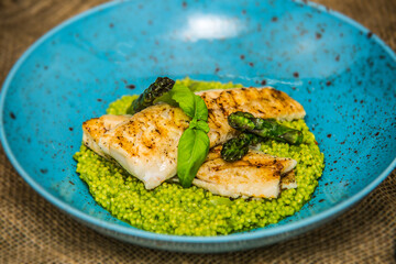 Fried fish fillet with green couscous and fresh asparagus served on plate. The food in the restaurant. Food styling and restaurant meal serving.