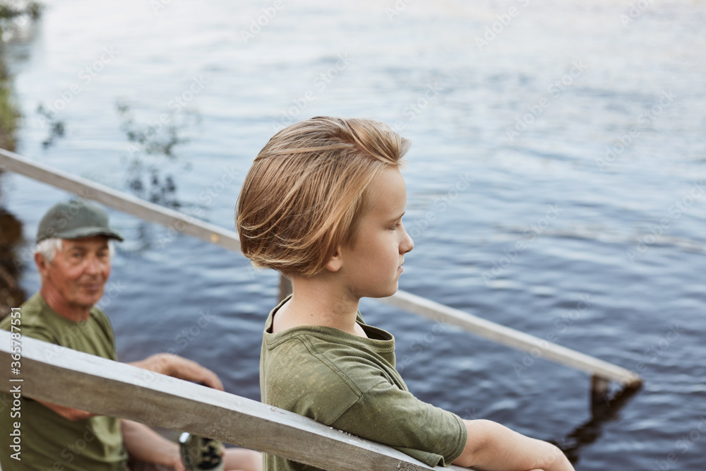 Wall mural Little boy with mysterious sight looking in distance, guy with grandfather posing on wooden stairs, family spending time together in open air, enjoying beautiful nature.