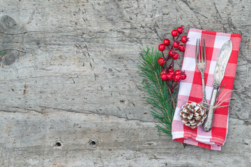 Fototapeta na wymiar Merrry Christmas background. Vintage fork and knife, holly berries and fir twig on checkered napkin and rustic wooden background. Space for text, flat lay