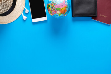 Top view of smartphone, globe model, black wallet, passport, and hat on blue background