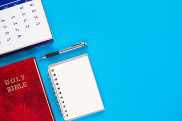 Top view of calendar, Holy Bible, and notebook on blue background