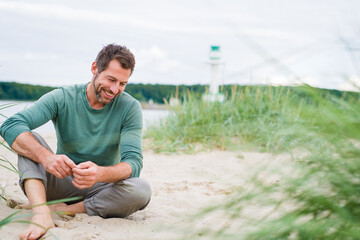 bestager Mann sitzt am strand und lächelt in sich hinein mit viel platz drumherum  