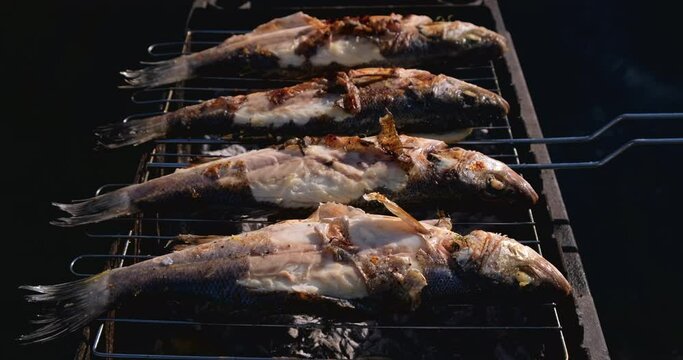 Sea bass or grouper fish grilled over charcoal. Close-up shot cooking seafish with aromatic spices on barbecue grill plate. Baking roasting marinated delicious seafood. BBQ  in summer garden outdoors 