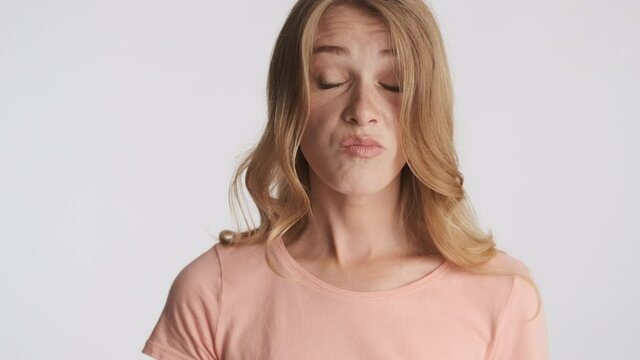 Young frustrated blond woman emotionally chewing on camera over gray background