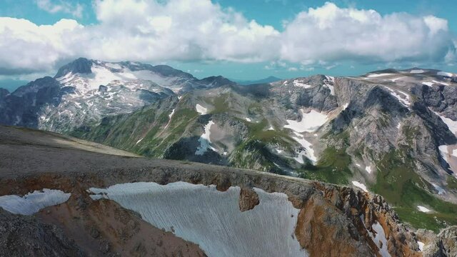 Aerial landscape view of beautiful Caucasian mountains covered snow under large steam of clouds in sunny weather in morning of summer, Adygea, Russia. Concept of travel, tourism and hike in mountain.