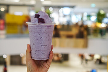 Murasaki Imo Smoothie. Woman holding a cup of Japanese purple sweet potato smoothie with blurred background.