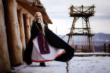 Beautiful blonde Viking dressed in a black cloak against the backdrop of the castle