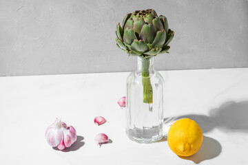 Modern minimal food still life. Artichoke in a bottle with lemon and garlic on white background
