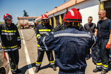 Group of firemen standing outdoors in protective uniforms and helmets and preparing for action.
