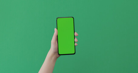 Young female hand hold smartphone with green screen on green background
