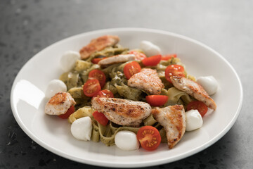 fettuccine with pesto, tomatoes , mozzarella and chicken on white plate