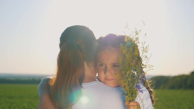 Happy family in the Park. A sweet girl embraces her mother and sister by the neck in the rays of the setting sun. Mom and daughter have fun spending their free time.