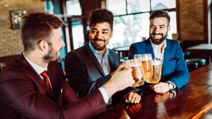 Cheerful old friends having fun and drinking beer at bar counter in pub.