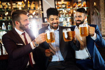 Happy young businessmen drinking beer and talking at pub after work