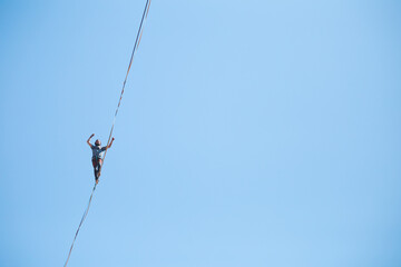 A man walks along the highline against the blue sky.