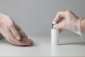 A jet of hydroalcoholic disinfectant gel shoots out of the bottle pressed by a gloved hand while...