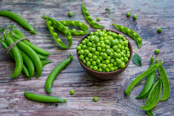 Fresh green peas in a bowl and pods on a rustic wooden table