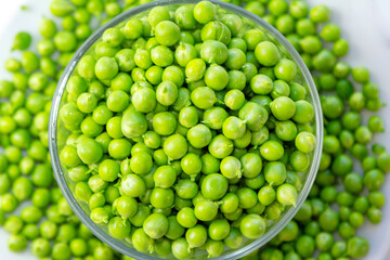 Close up fresh green peas in a glass bowl and pods on a white background