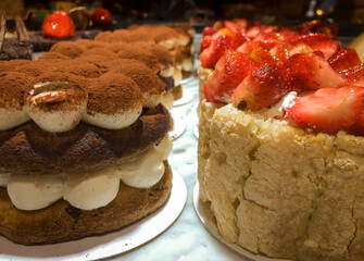 Close up of Turkish made deserts displayed on the window of a pastry shop. The one on the right is made up of bitter almond and strawberries while the left one if with cacao and cream.