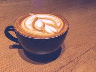 Top view close up shot of black coffee cup with heart shape latte art foam on wooden table. Delicious. Good morning. Start of the day with a latte or coffee. Cinematic look.