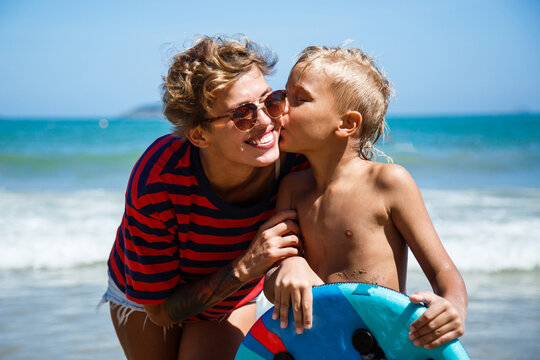 Mom and son look each other and smile, on the beach. Portrait of a woman and a boy against seashore.