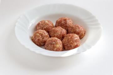 Raw meat balls with rice, spices, sauce, finely chopped cabbage are ready for cooking. A few raw noisettes lie on a white plate.