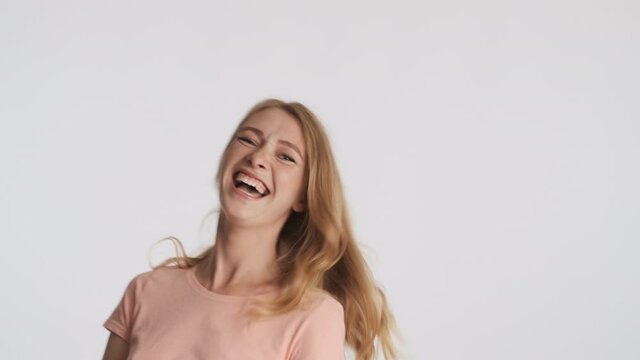 Young cheerful blond woman joyfully laughing on camera over gray background. Happy expression