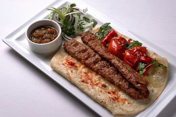 Lamb lula kebab, with baked tomatoes, onions and sauce, on a white plate, on a white background