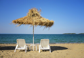 A straw umbrella with deck chairs on a sandy beach by the sea.