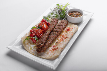 Lamb lula kebab, with baked tomatoes, onions and sauce, on a white plate, on a white background