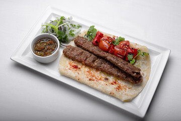 Lamb lula kebab, with baked tomatoes, onions and sauce, on a white plate, on a white background
