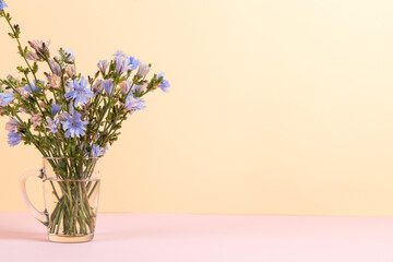 Blue flowers in a glass cup on a yellow pink background. Copy space.