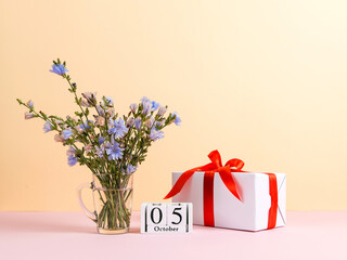 Flowers in a glass cup, gift and calendar with date of October 5, on a colored yellow pink background, Teacher's Day concept. Copy space.