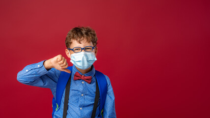 excited boy in mask, glasses, with school backpack shows gesture of disapproval.