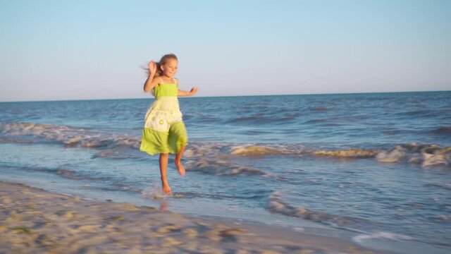 A cheerful girl in a sundress runs barefoot along the coast to meet the rising sun. Holidays at sea or ocean. Feelings of joy and pleasure.